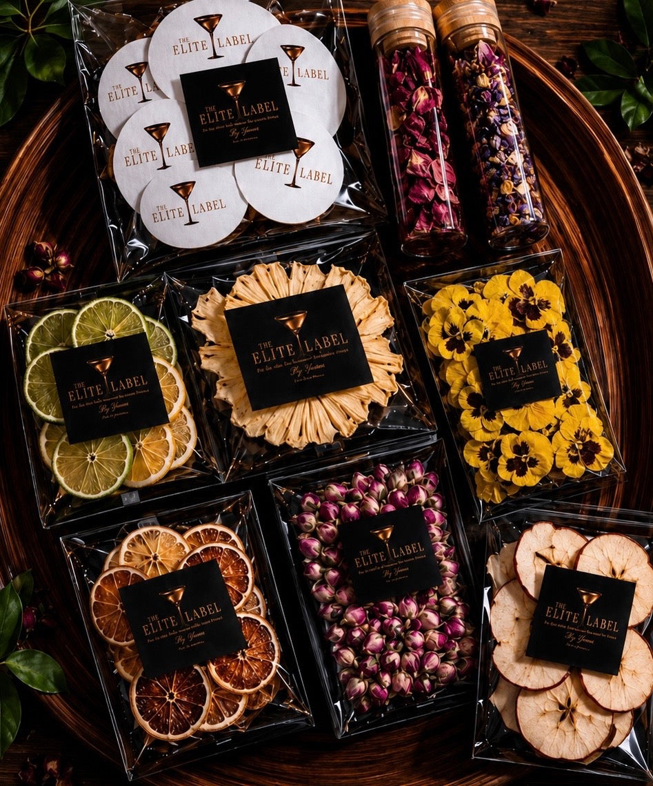 Assorted packaged dried fruit and flower cocktail garnishes with 'Elite Label' branding on a wooden surface.