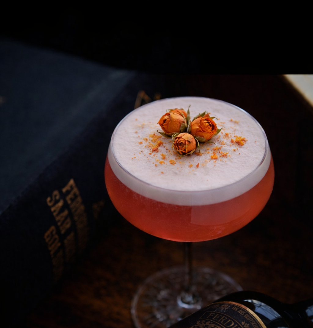 Cocktail with orange flower garnishes in a glass, placed on a dark surface