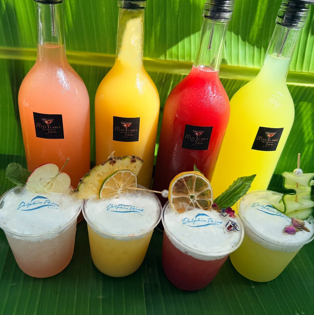 Assorted colorful fruity cocktail drinks with fruit garnishes in matching glasses on a green leaf background