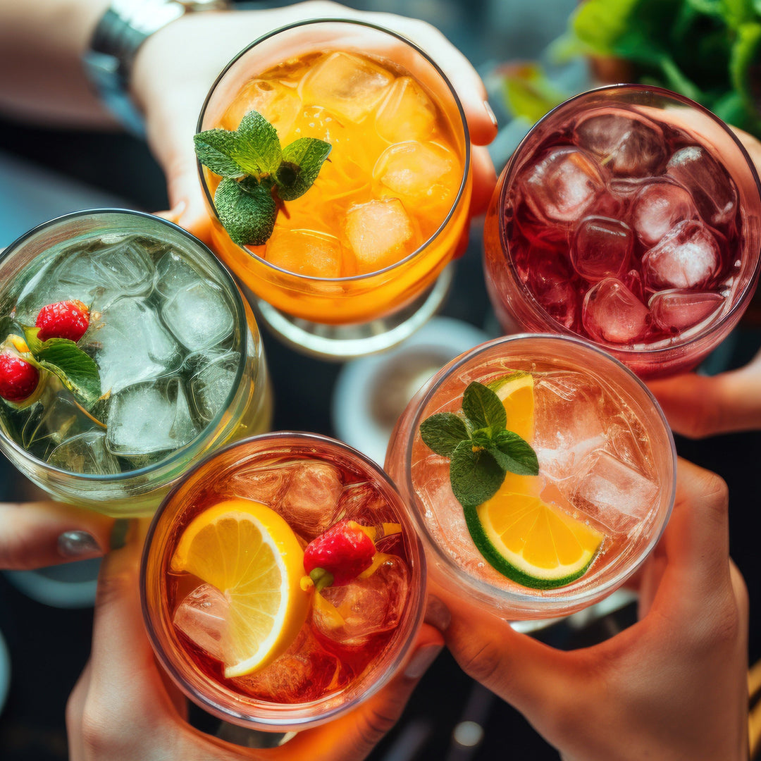 Five glasses of iced drinks with garnishes held by people in a celebratory manner.