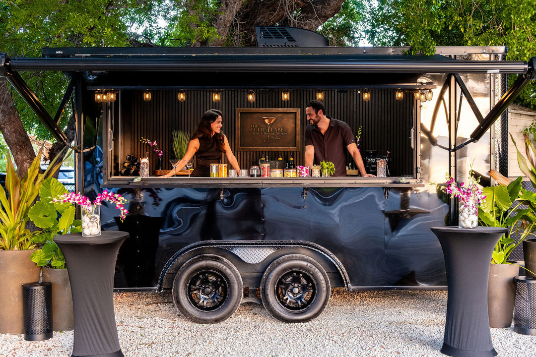 Mobile bar truck with two bartenders behind the counter, surrounded by plants.