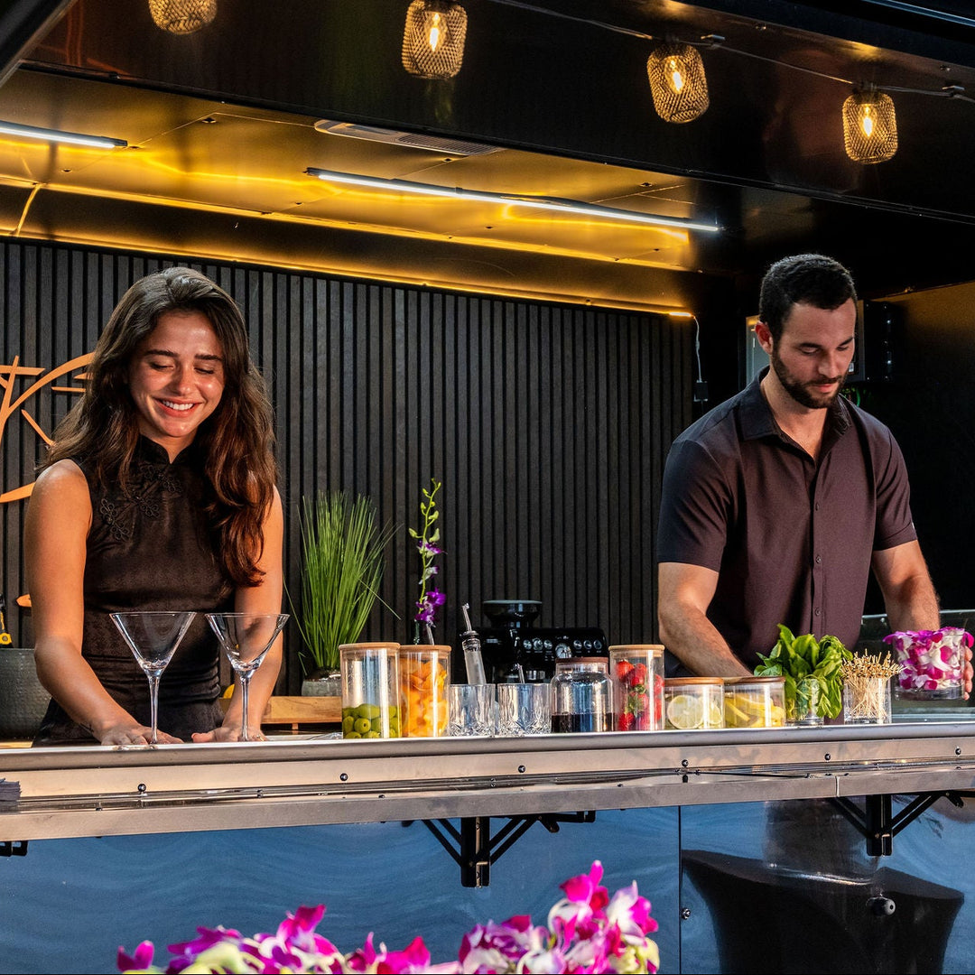 Two bartenders preparing drinks at a  mobile bar counter with decorative elements.