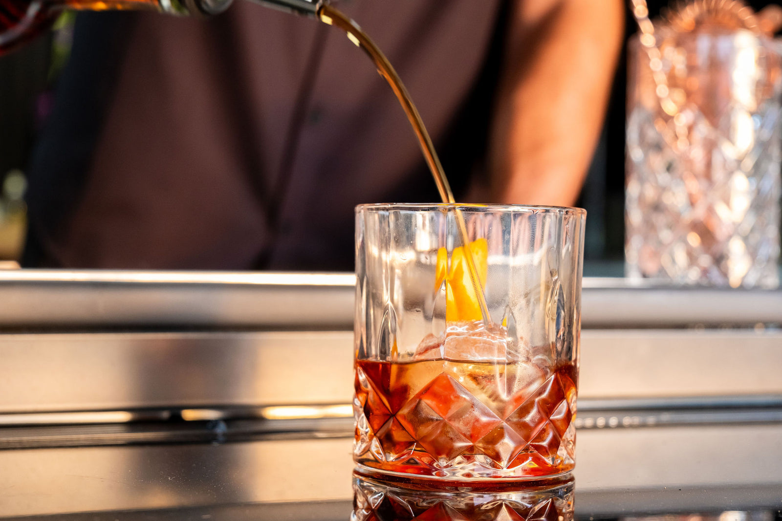 Alcoholic drink being poured into a glass with ice cubes on a mobile bar counter.