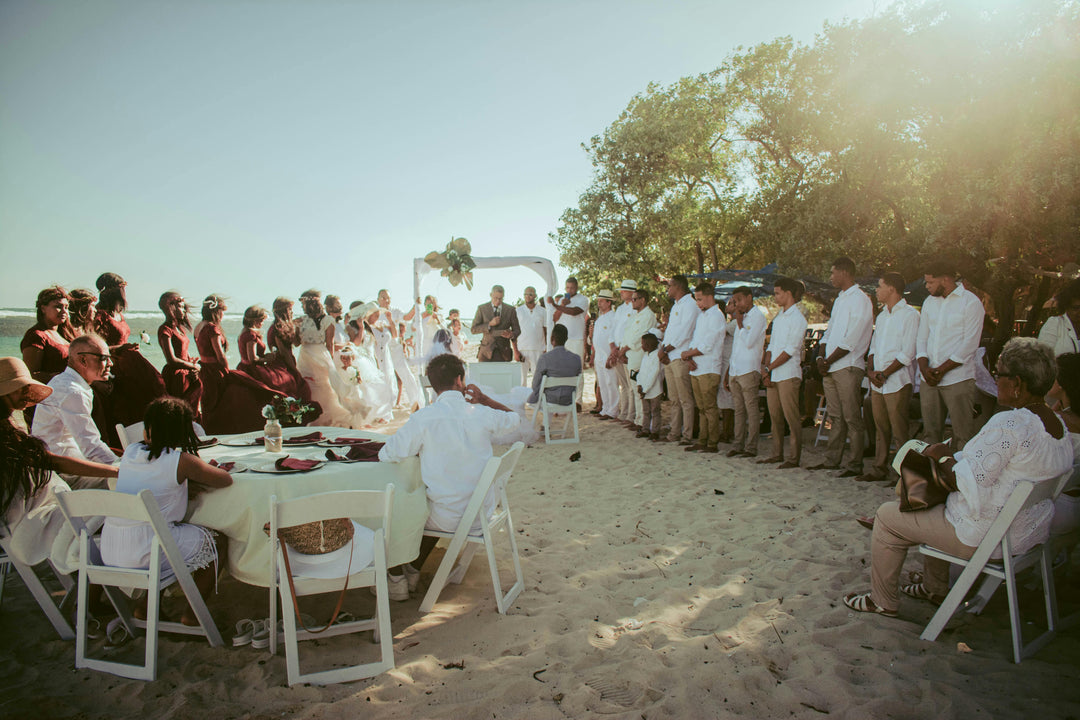 Group of people gathered for a ceremony on a sandy beach with trees in the background.