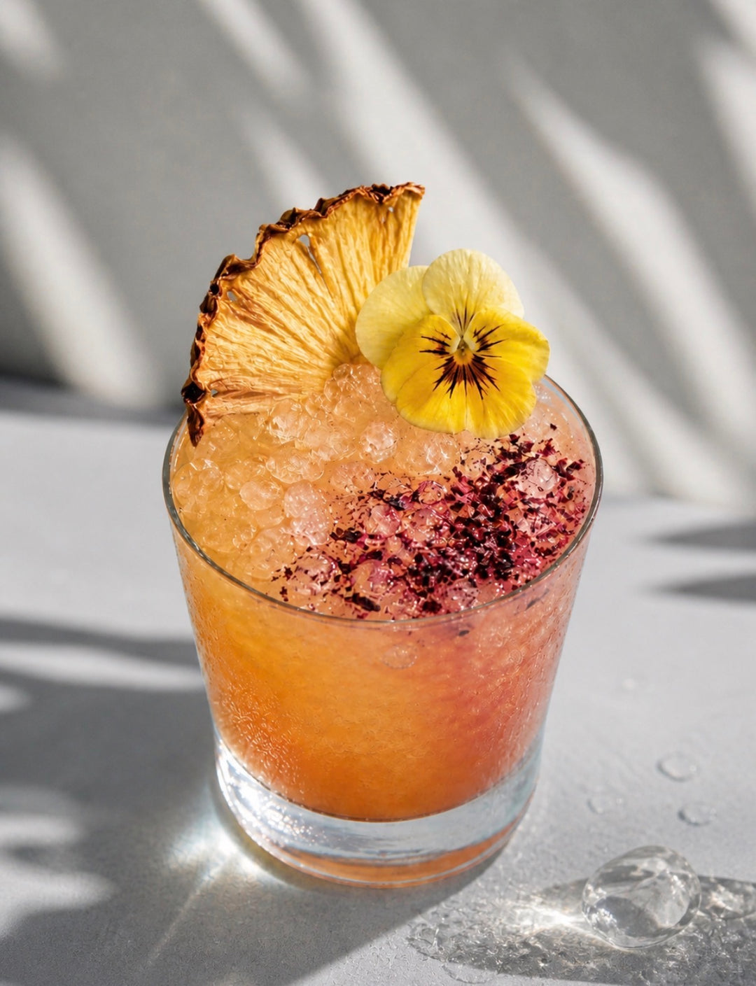 Cocktail with dehydrated pineapple garnish and yellow flower on a light background
