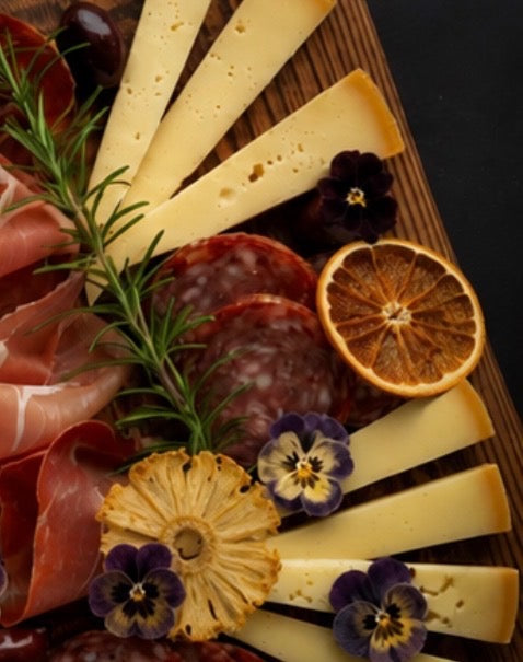Platter of sliced cheese, cured meats, and dried fruits with garnishes on a wooden board.