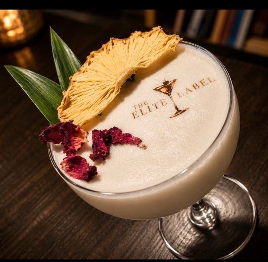 Cocktail with pineapple wedge and dried flowers in a glass with an edible cocktail topper that says &