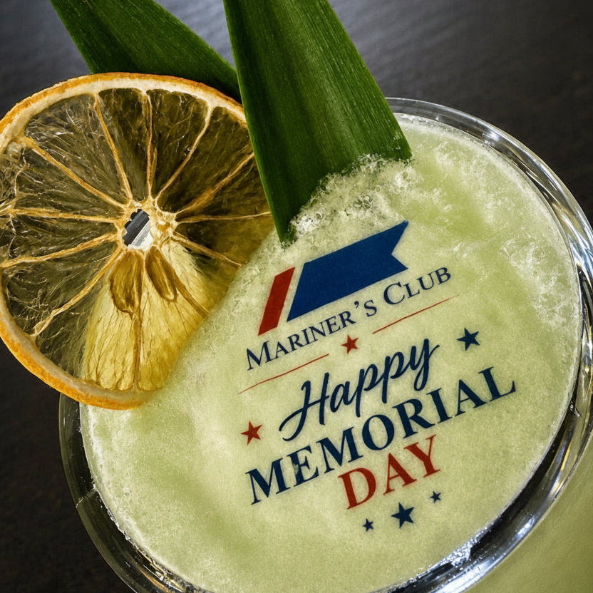 Cocktail with lemon slice and garnish, featuring 'Mariner's Club' edible cocktail topper that says 'Happy Memorial Day' text.