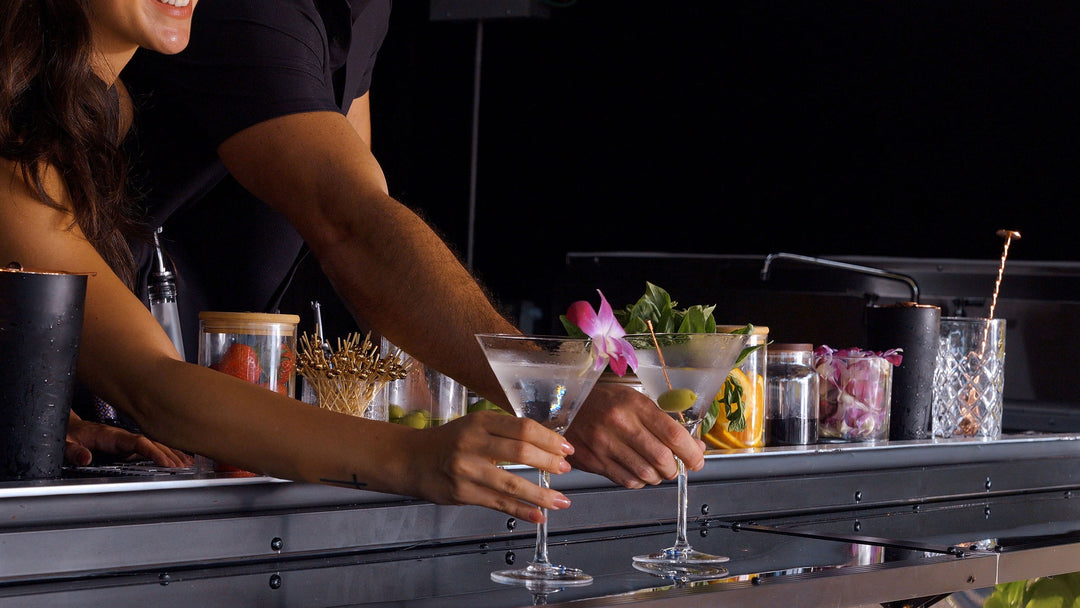 Bartender preparing a cocktail at a mobile bar with various garnishes and cocktail glasses.