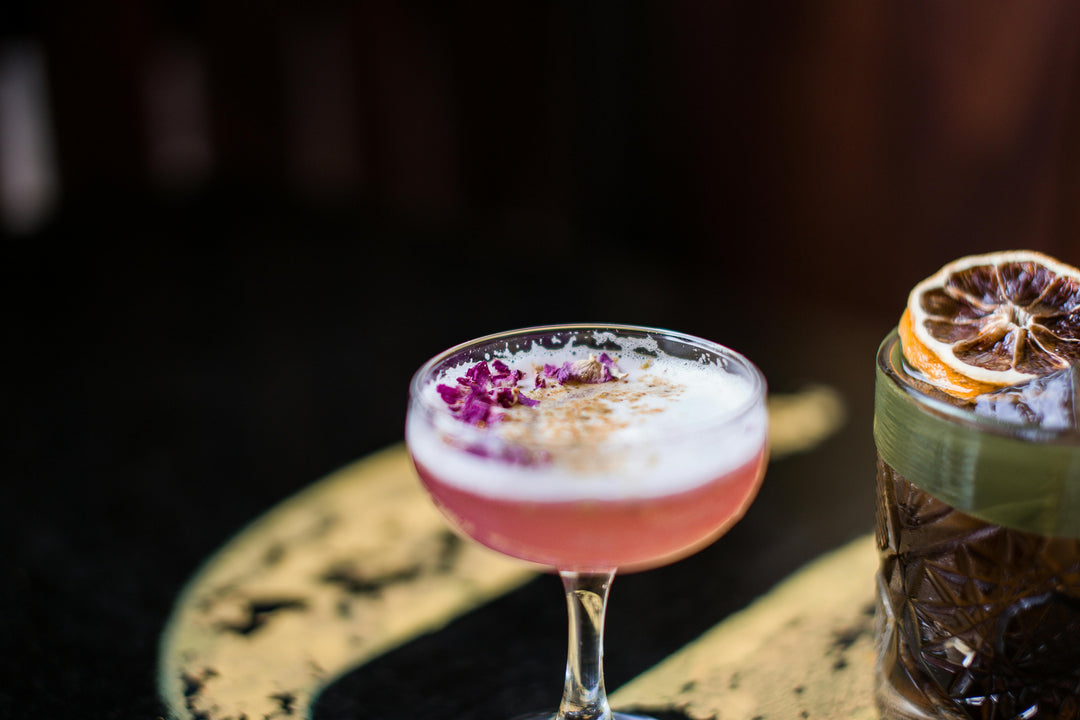 Cocktail with a pink foam and garnish on a dark background