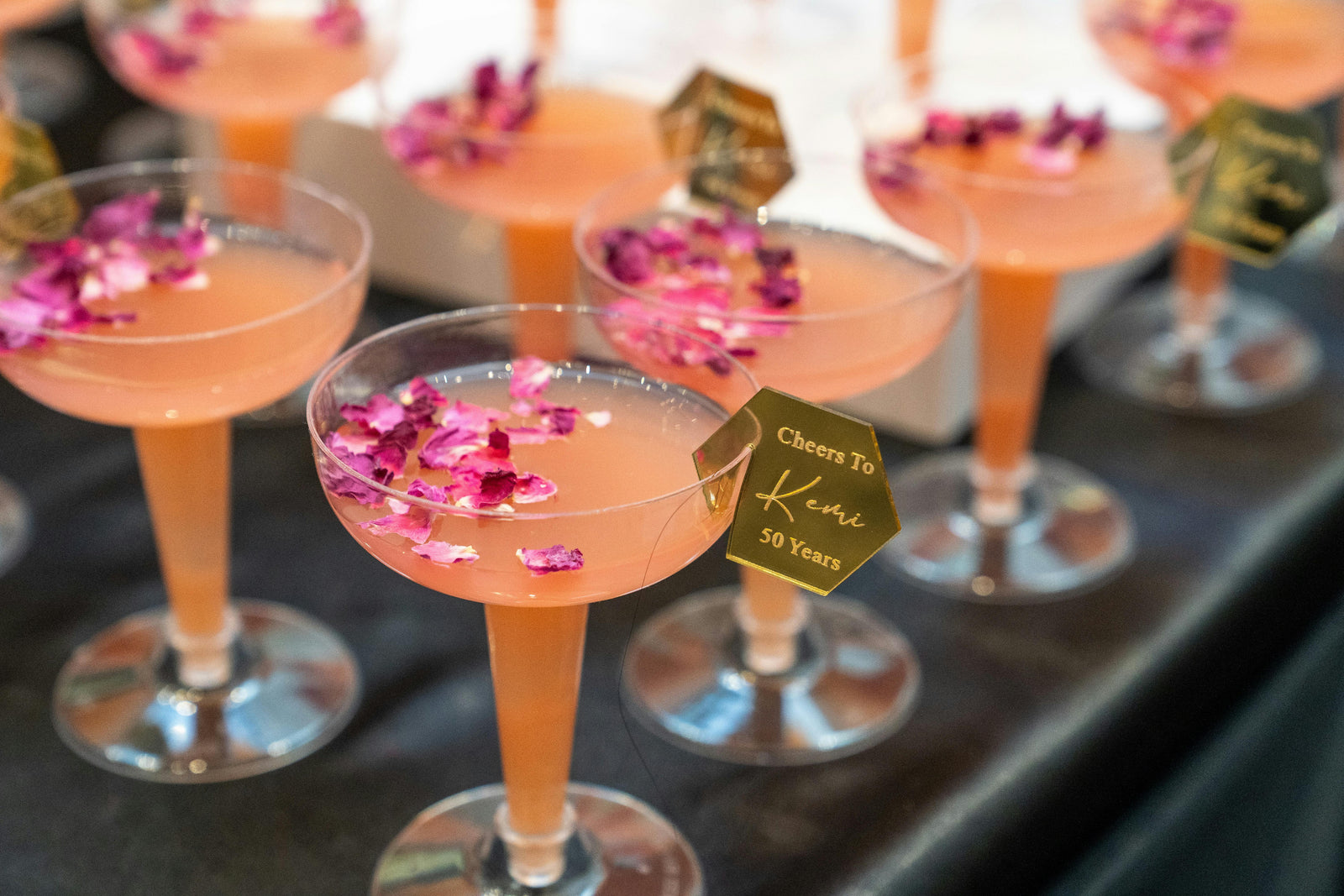 Cocktails in glasses with pink rose petals and a 'Cheers To 50 Years' tag.