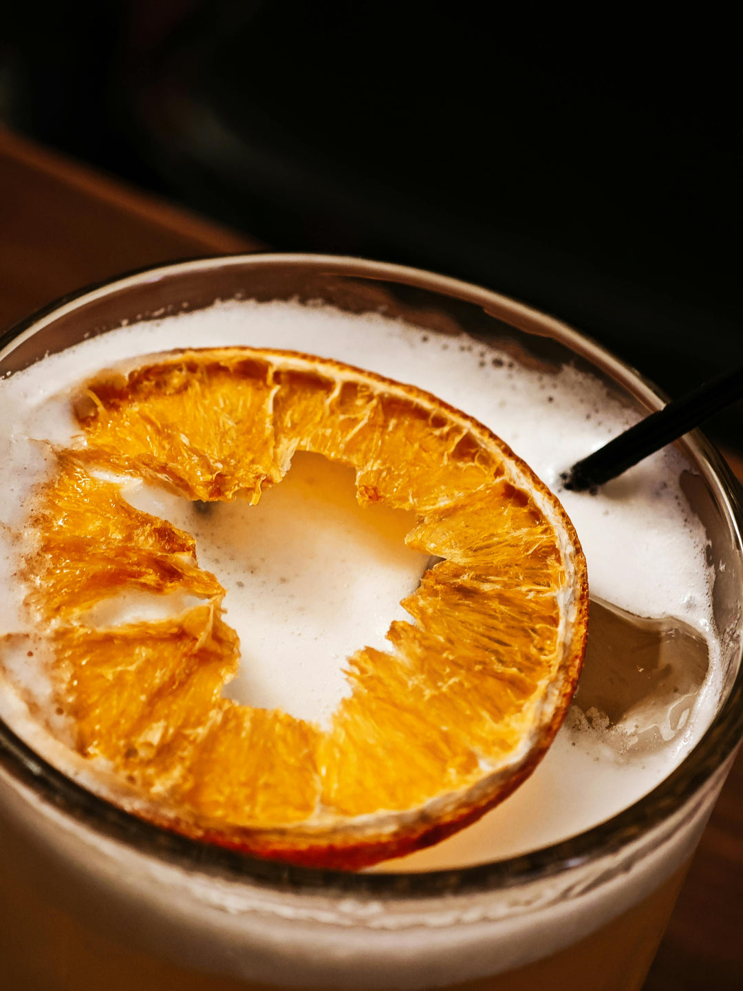 Close-up of a cocktail with a dried orange wheel and a black straw on a dark background